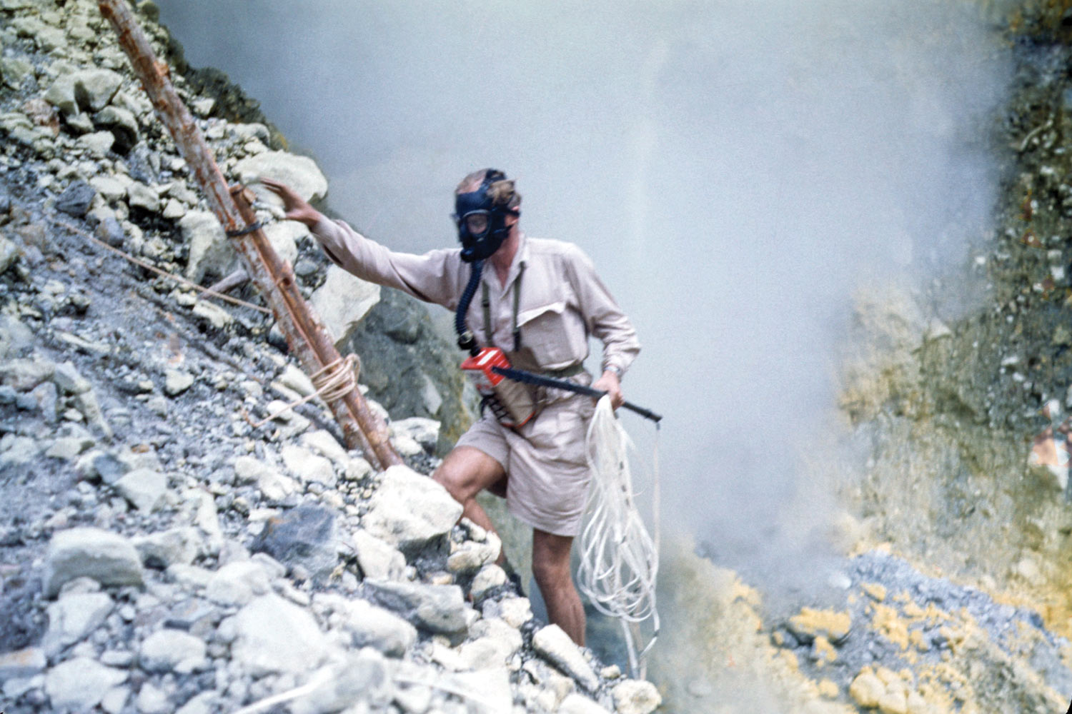 A man wearing breathing apparatus climbs a makeshift ladder down a rocky cliff.