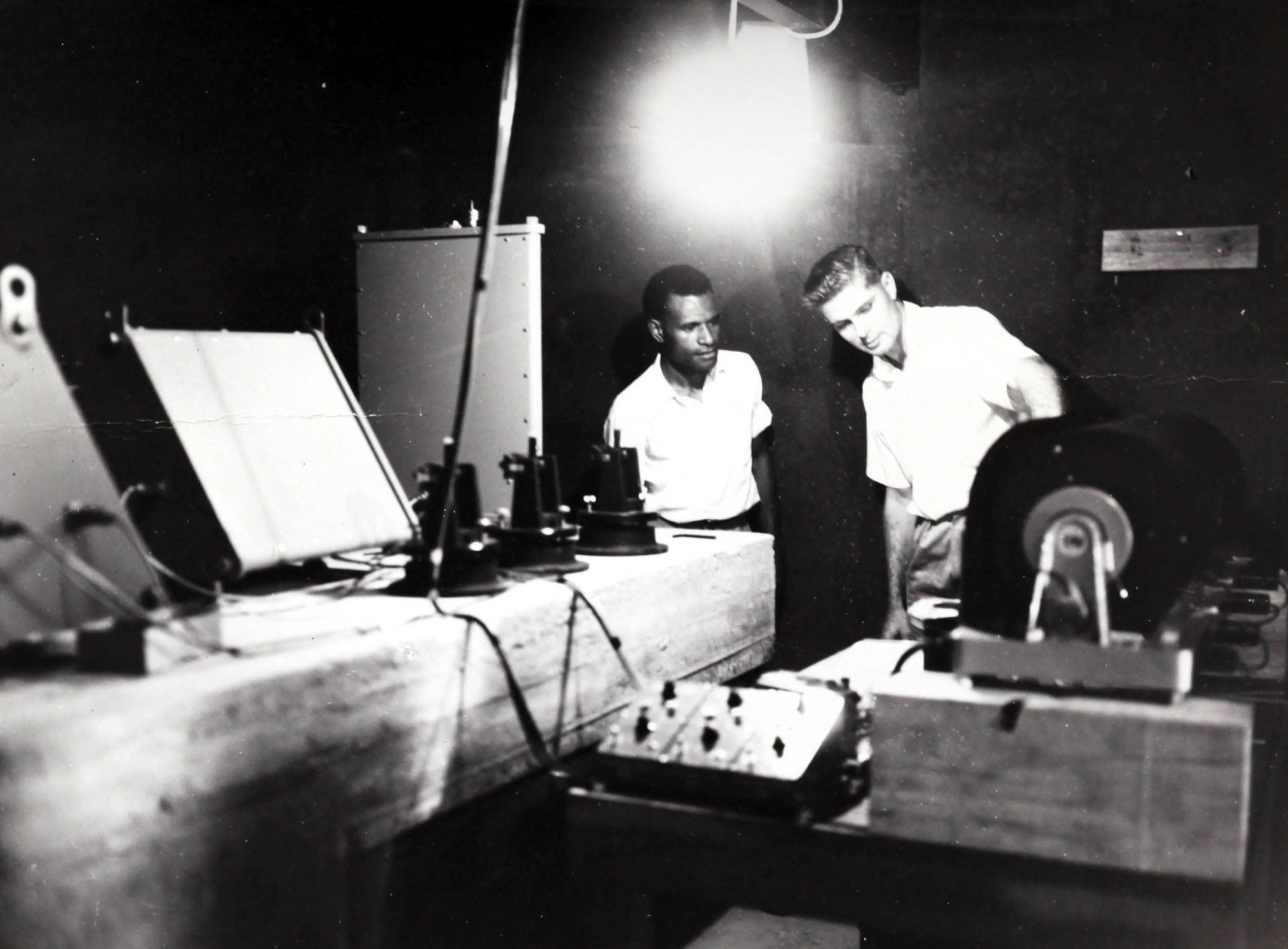 Black and white image showing two men examining some scientific equipment.