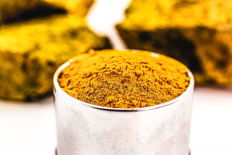 Powdered yellow uranium oxide in a container with yellowcake uranium chunk in the background