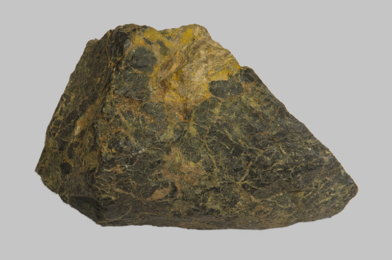 A green-grey coloured rock is covered in yellow coloured striations. The top is also yellow.