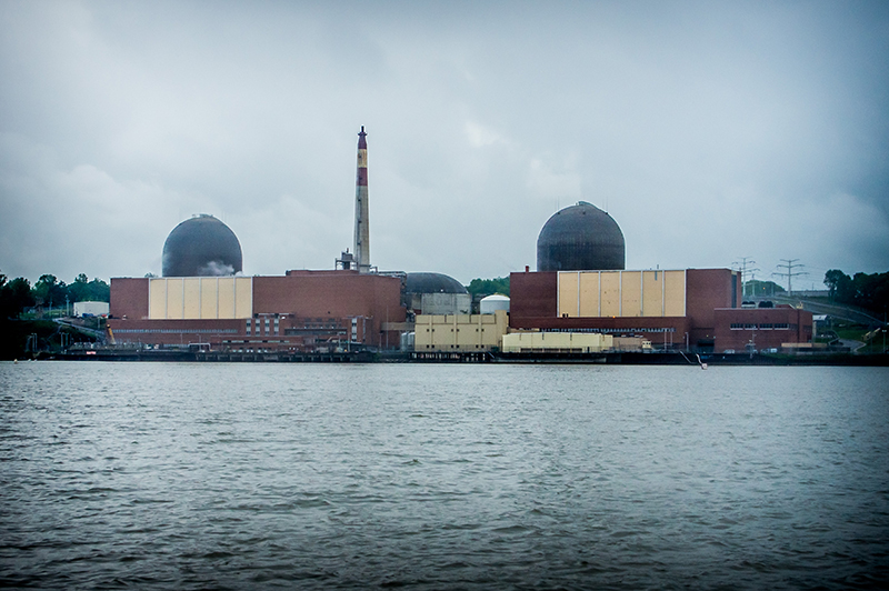 Two large rectangular building with domes on top sit on the shore of a water body. A large chimne poke out of one of the buildings.