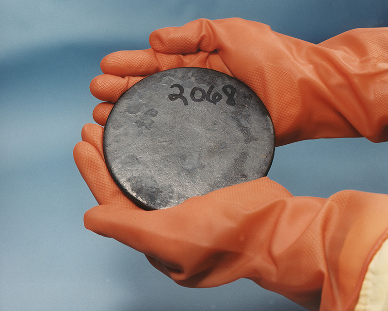 A round disc of metal is being held in gloved hands.