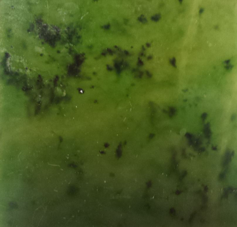 A slab of light green coloured jade with dark coloured patches.