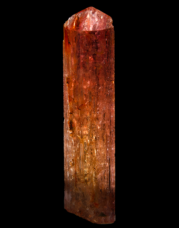 A red coloured topaz crystal with vertical striations and orange and black inclusions in it