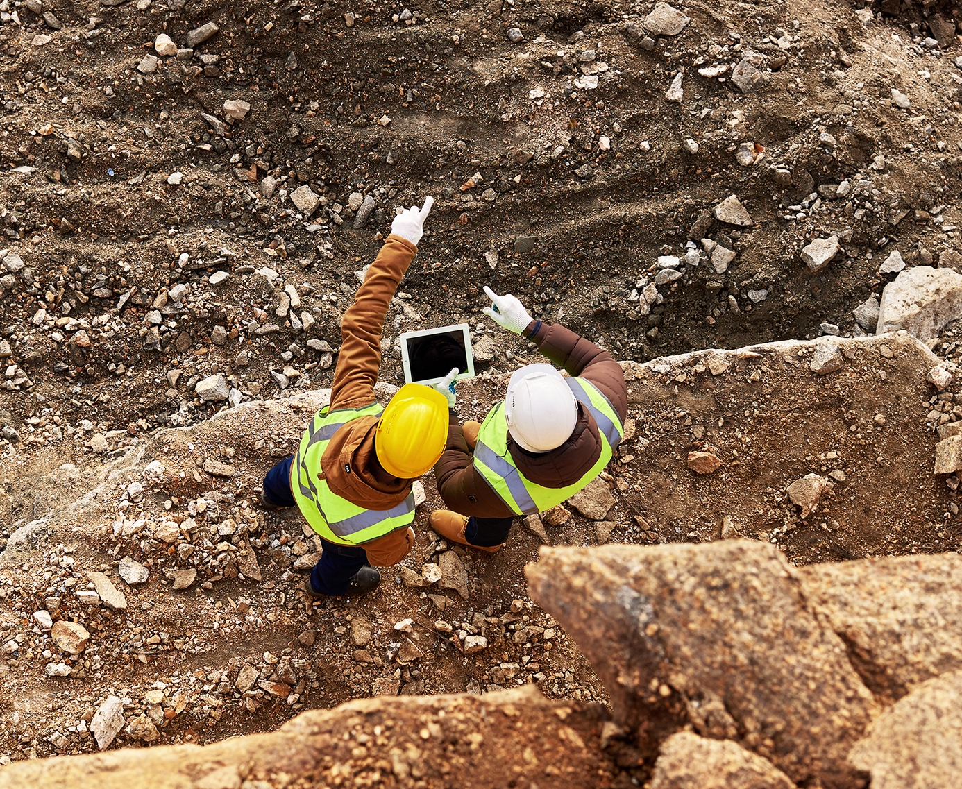 Aerial view of two people with hardhats and a tablet computer in a mine site pointing to distance